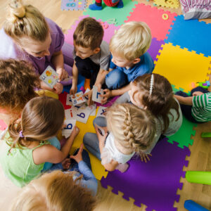 Group of kindergarten kids sitting closely on a floor together with teacher, providing group work. Children learning to cooperate while solving tasks.